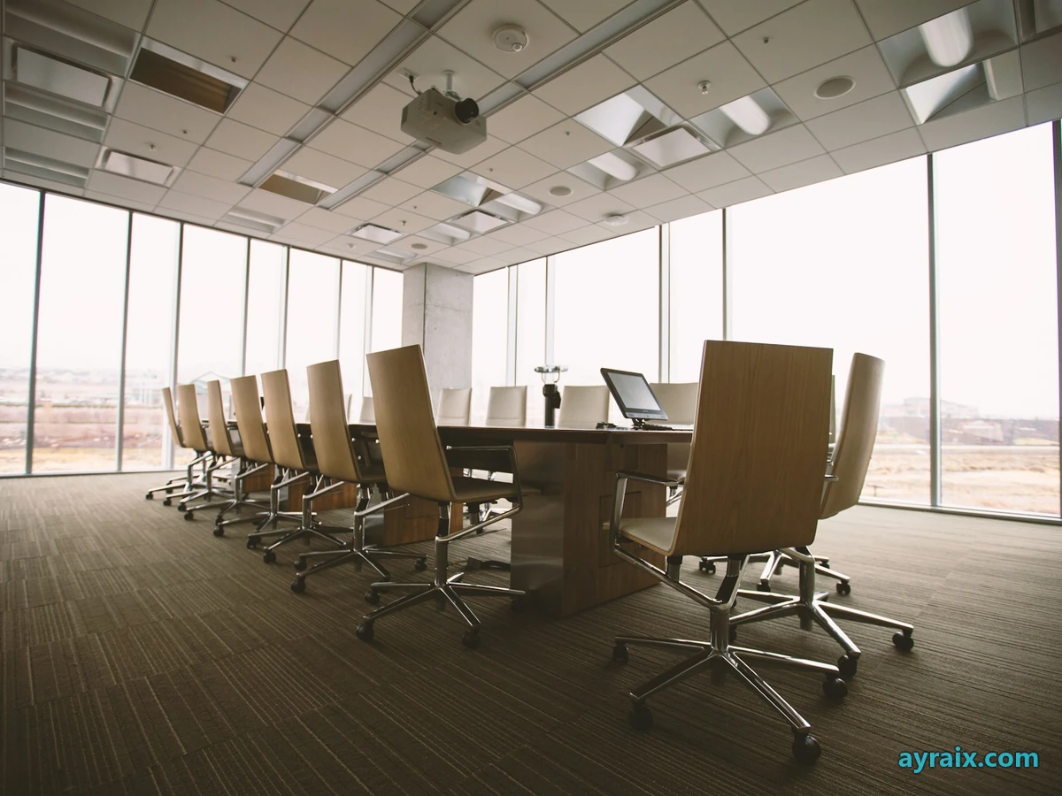 Empty glass-walled boardroom with a long conference table and daylight through floor-to-ceiling windows
