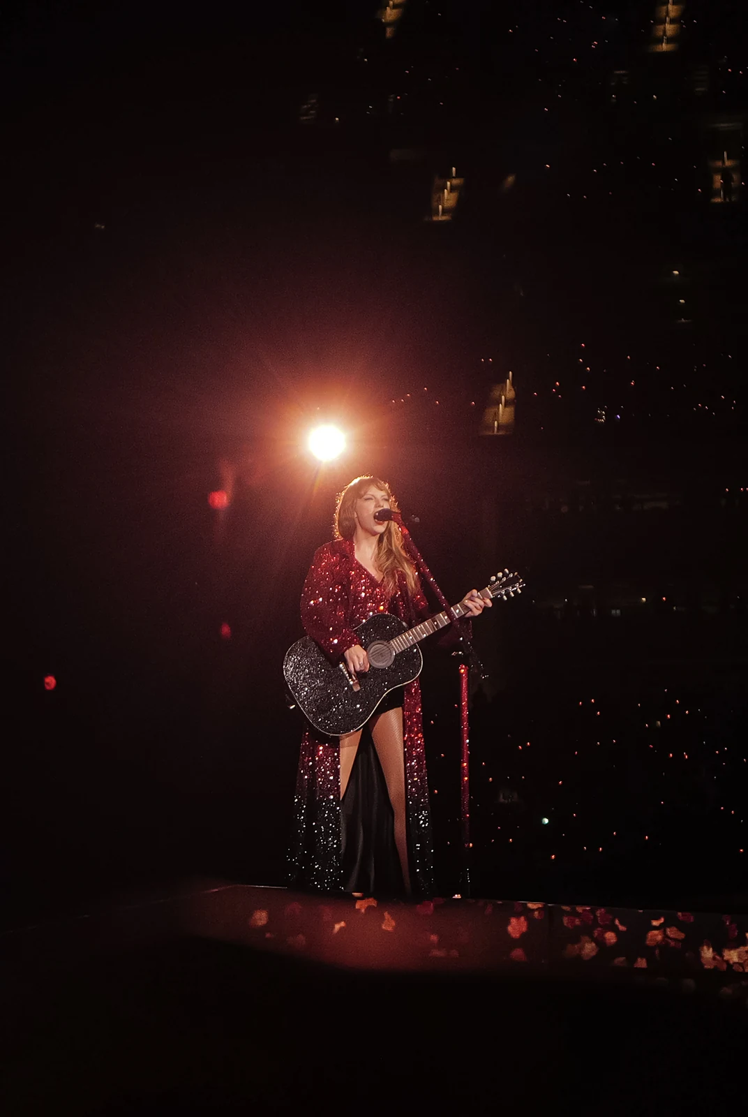 Taylor Swift in the Red era set of The Eras Tour in Inglewood, playing guitar under stadium lights