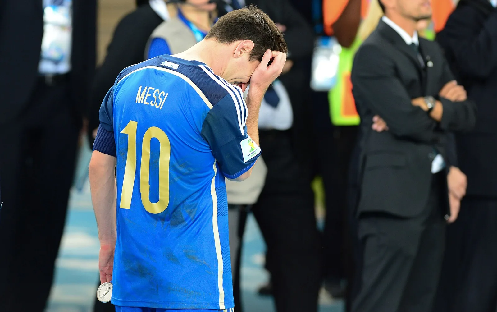 Lionel Messi holding a silver medal, hand covering his face in tears after a World Cup final loss