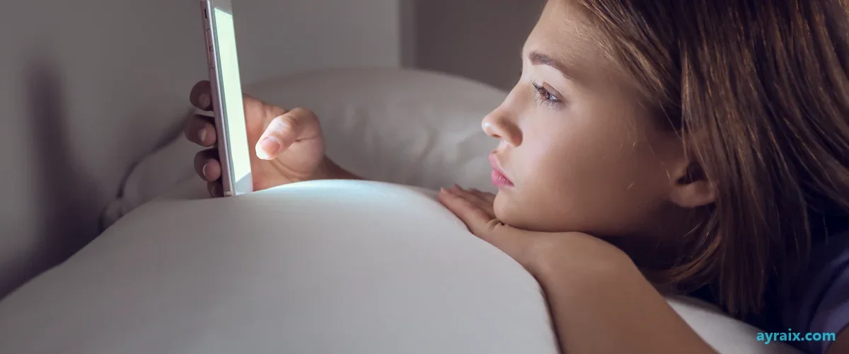 A teenage girl alone at night, lit only by her phone screen, absorbed in the feed