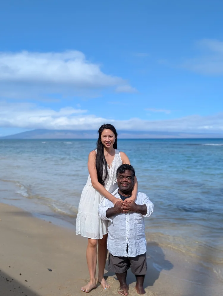 Anita Wing Lee and Tim Muttoo standing together on a beach, her hands on his shoulders