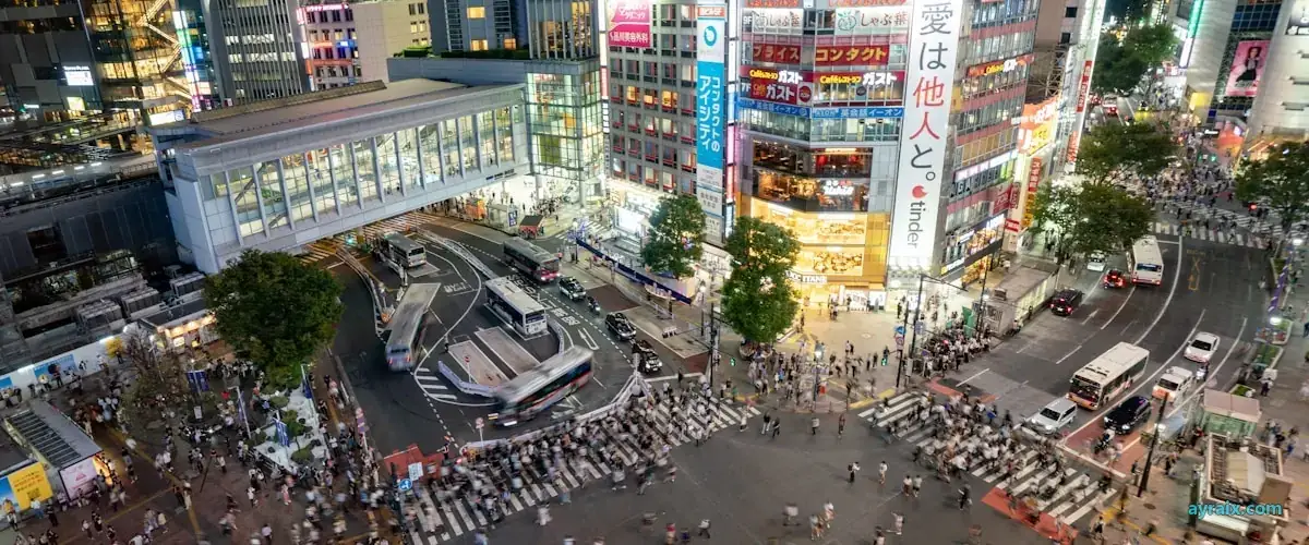 Aerial view of a dense, brightly lit city crossing packed with people at night