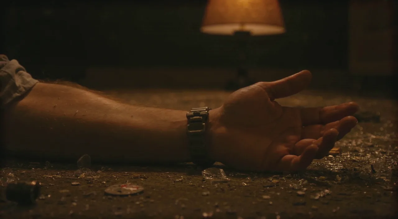 An open palm on a debris-covered floor, a broken watch on the wrist