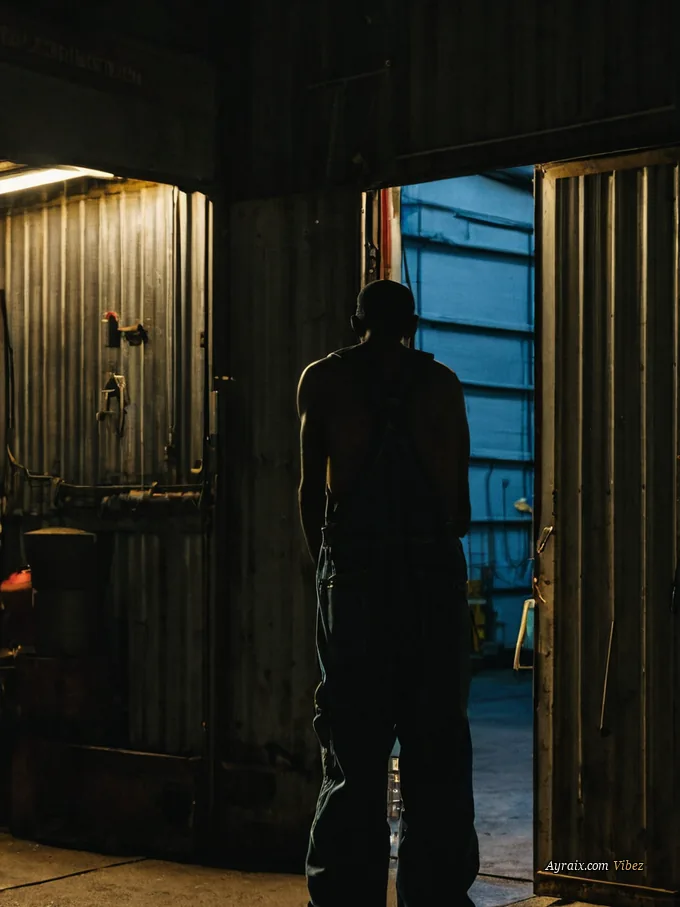 A machine shop doorway at night, warm light spilling onto the pavement.